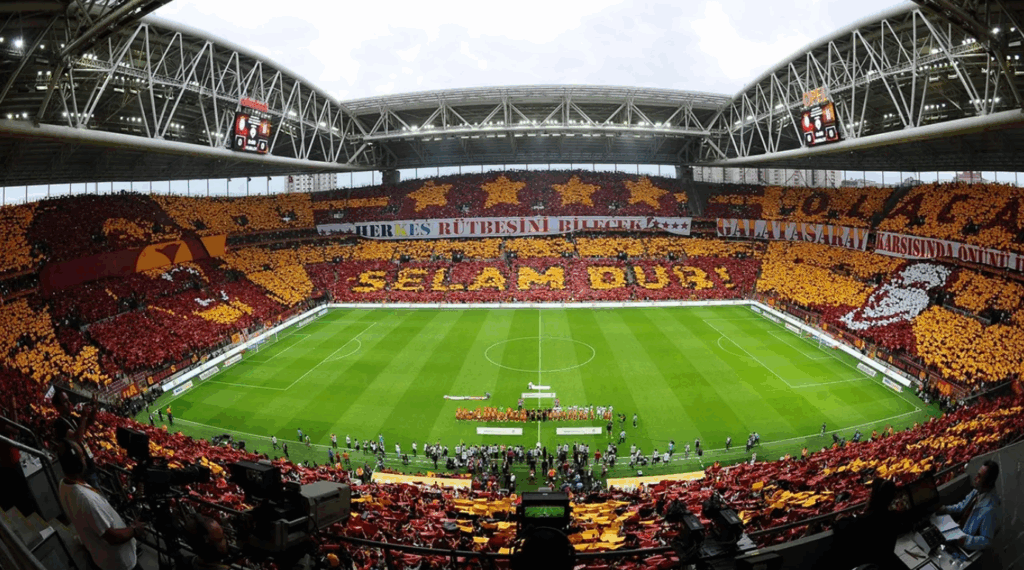 Fans of Galatasaray 2025 Süper Lig Champions create a five-star crest choreography with red and yellow flags at RAMS Park under a starry Istanbul sky.
