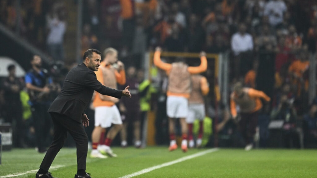 Okan Buruk directs the Galatasaray 2025 Süper Lig Champions from the sidelines at RAMS Park, with fans waving red and yellow flags under floodlights.
